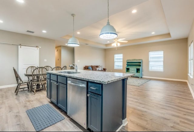 kitchen with a barn door, a raised ceiling, dishwasher, light wood-type flooring, and a sink