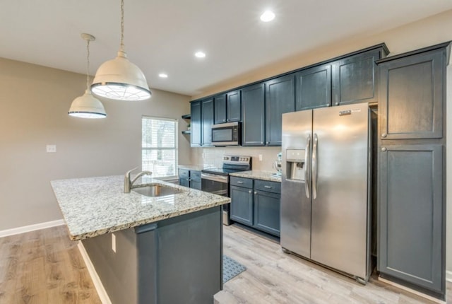 kitchen with light stone counters, a sink, appliances with stainless steel finishes, light wood finished floors, and a center island with sink