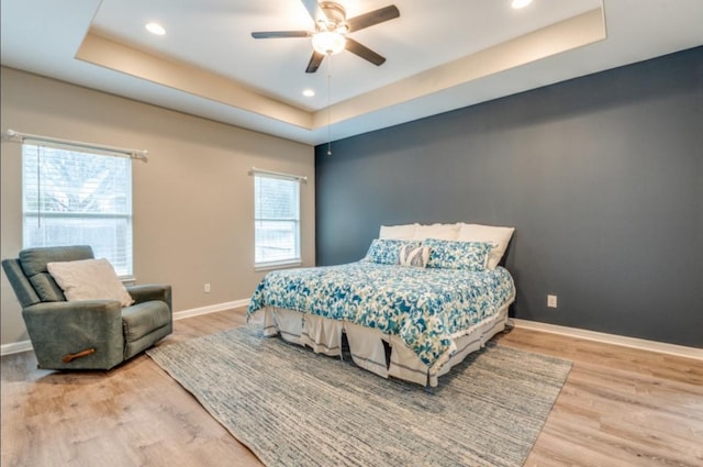 bedroom with recessed lighting, a raised ceiling, baseboards, and wood finished floors