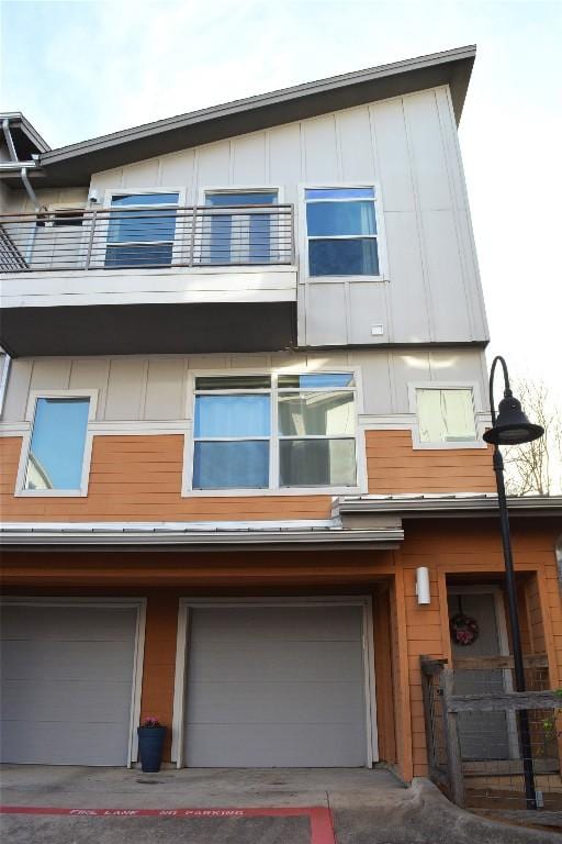 view of side of property featuring board and batten siding, driveway, a balcony, and an attached garage