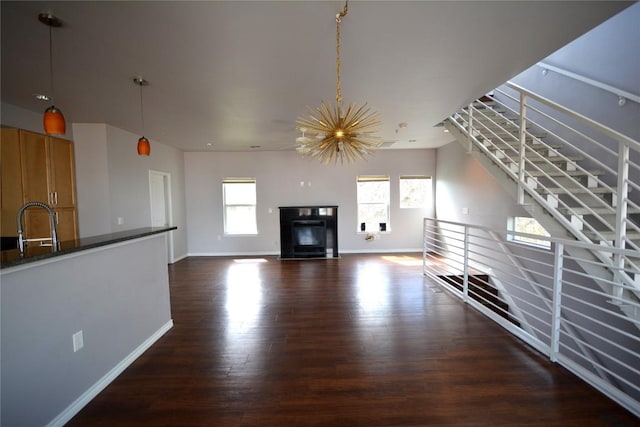 unfurnished living room with a glass covered fireplace, dark wood finished floors, baseboards, and an inviting chandelier