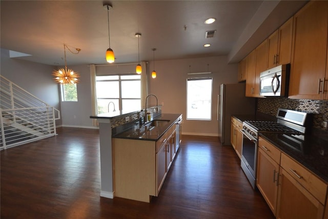 kitchen featuring a sink, appliances with stainless steel finishes, dark wood-style floors, tasteful backsplash, and a center island with sink