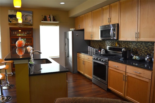 kitchen featuring a center island with sink, tasteful backsplash, appliances with stainless steel finishes, dark wood-type flooring, and a sink