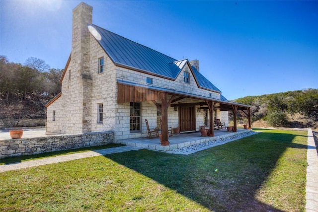 rear view of property featuring a standing seam roof, metal roof, a chimney, and a lawn