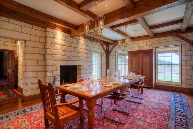 dining area with a stone fireplace, wood finished floors, beam ceiling, and an inviting chandelier