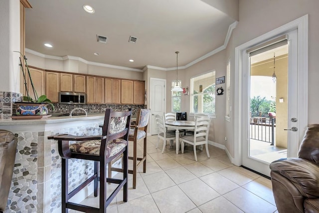 kitchen with light tile patterned flooring, visible vents, ornamental molding, decorative backsplash, and stainless steel microwave