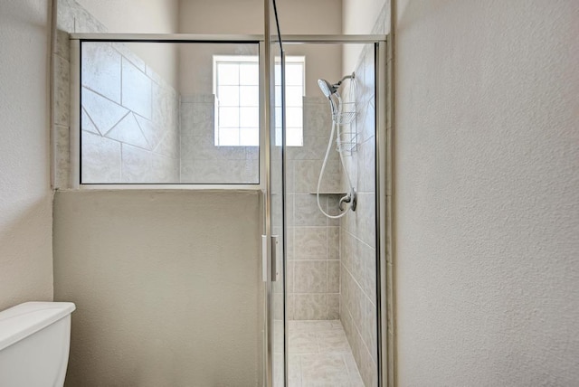 full bath featuring a textured wall, a shower stall, and toilet