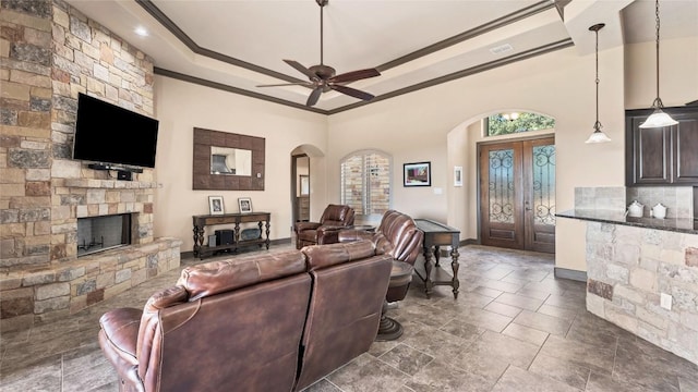 living room with arched walkways, a raised ceiling, crown molding, french doors, and a fireplace