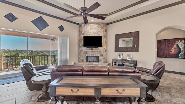 living area featuring ceiling fan, a stone fireplace, ornamental molding, a raised ceiling, and stone tile flooring