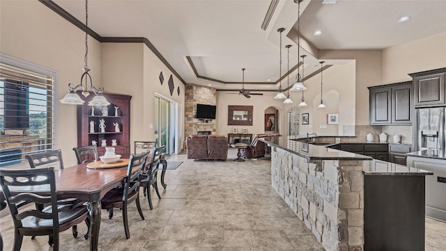 kitchen with arched walkways, ceiling fan, dark stone countertops, crown molding, and stainless steel refrigerator with ice dispenser