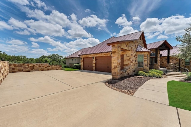 view of property exterior with metal roof, an attached garage, stone siding, driveway, and a standing seam roof