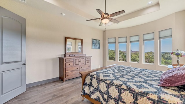 bedroom featuring light wood-style floors, a raised ceiling, and baseboards