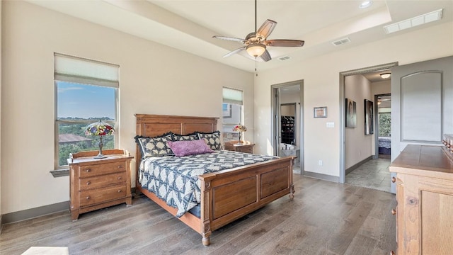 bedroom featuring a tray ceiling, visible vents, baseboards, and wood finished floors