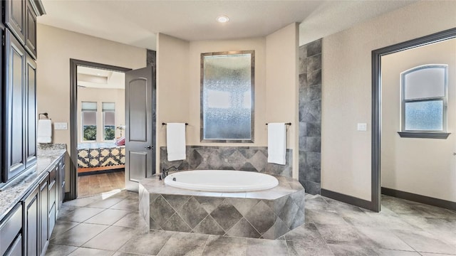 ensuite bathroom featuring a bath, tile patterned flooring, a wealth of natural light, and baseboards