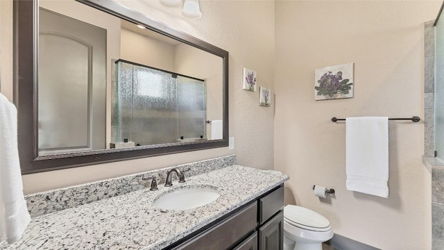 full bath with a textured wall, a shower with door, vanity, and toilet