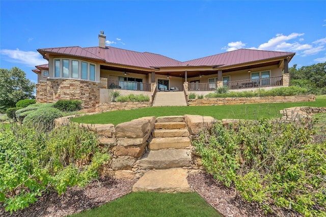 rear view of property featuring metal roof, stone siding, a chimney, and stucco siding