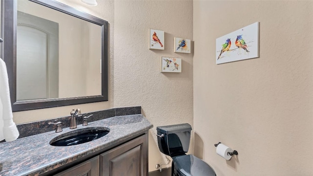 half bath with a textured wall, vanity, and toilet