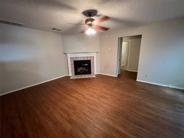 unfurnished living room featuring baseboards, visible vents, a ceiling fan, dark wood finished floors, and a tiled fireplace