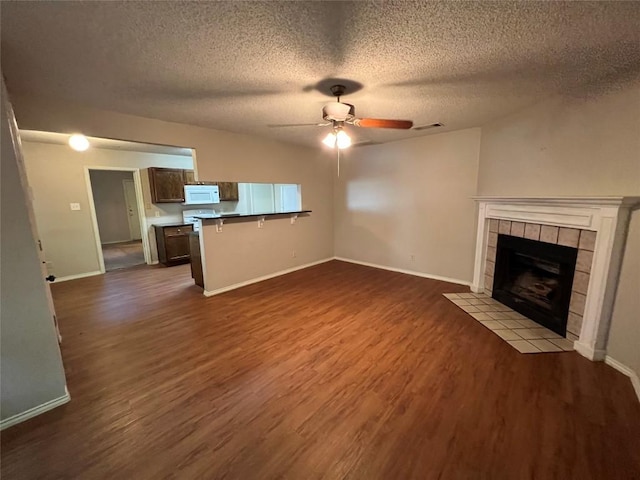 unfurnished living room with dark wood-type flooring, baseboards, a tiled fireplace, and a ceiling fan