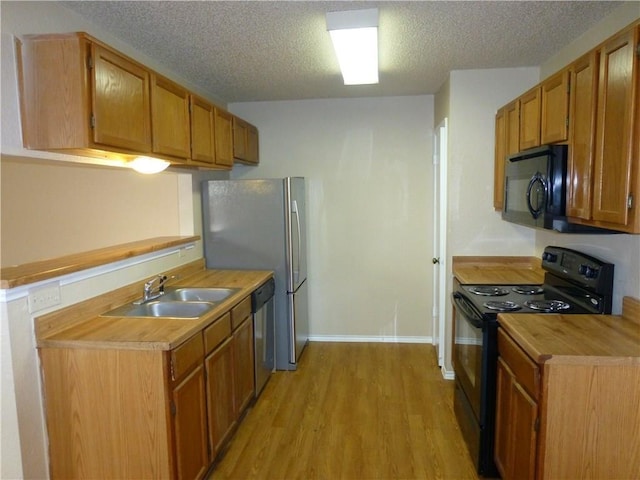 kitchen featuring a textured ceiling, black appliances, a sink, and light wood-style floors