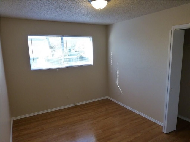 spare room featuring a textured ceiling, baseboards, and wood finished floors