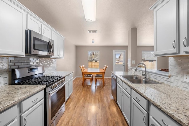 kitchen with stainless steel appliances, visible vents, light wood-style flooring, a sink, and baseboards