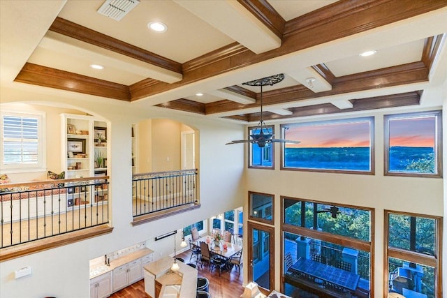 interior space featuring visible vents, coffered ceiling, beamed ceiling, wood finished floors, and crown molding