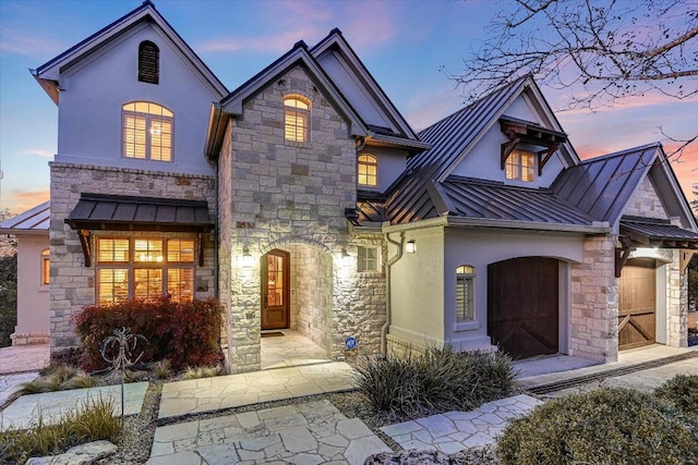 view of front of house with a garage, stone siding, metal roof, a standing seam roof, and stucco siding