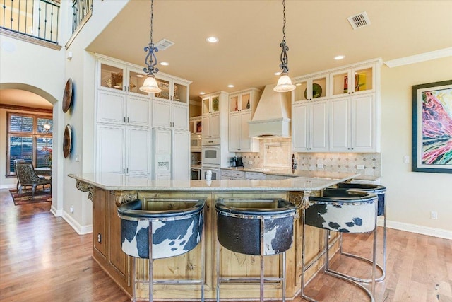 kitchen featuring arched walkways, visible vents, light wood-type flooring, tasteful backsplash, and custom range hood