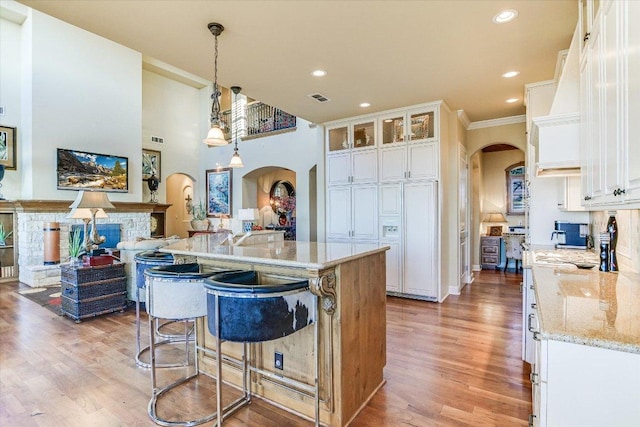 kitchen with light wood finished floors, a kitchen bar, arched walkways, and white cabinets