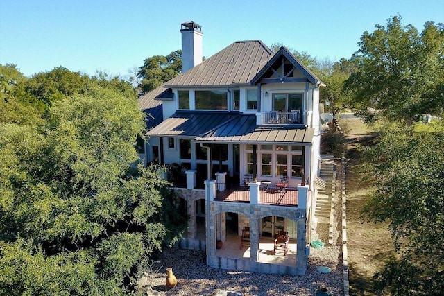 rear view of property featuring a standing seam roof, a patio area, metal roof, a balcony, and stone siding