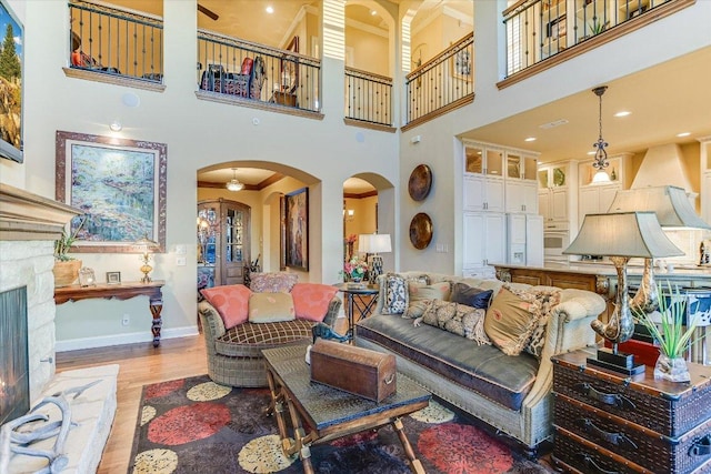 living area featuring baseboards, a lit fireplace, arched walkways, and wood finished floors