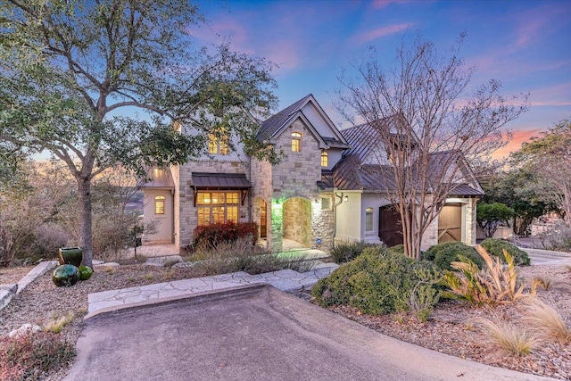 view of front of house featuring stucco siding, an attached garage, a standing seam roof, metal roof, and stone siding