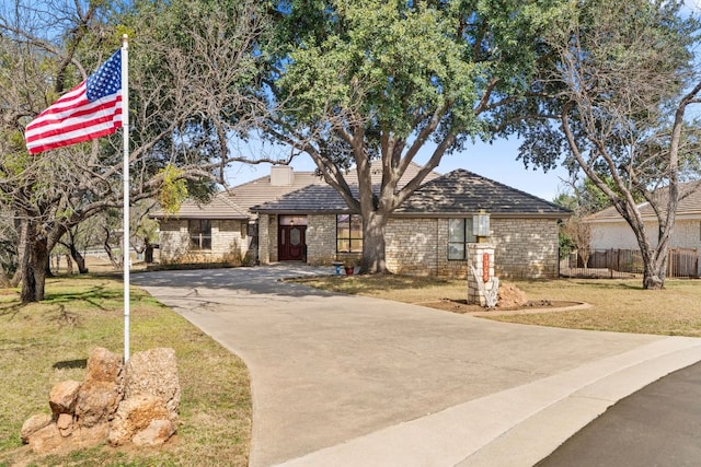 view of front facade with fence, concrete driveway, stone siding, a chimney, and a front yard