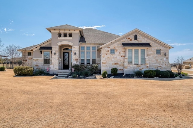 view of front facade with stone siding, a front yard, and roof with shingles