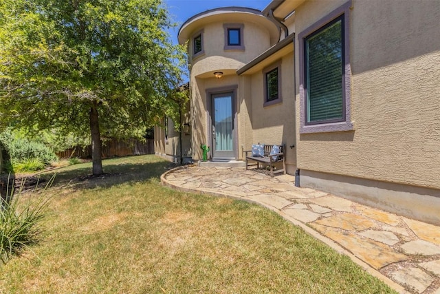 view of exterior entry featuring a yard, fence, a patio, and stucco siding