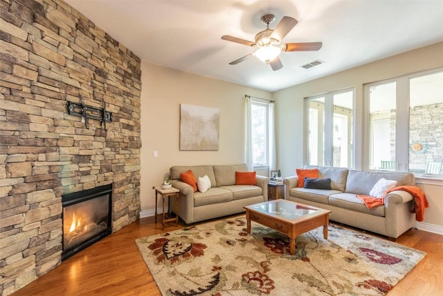 living room with plenty of natural light, visible vents, wood finished floors, and a stone fireplace