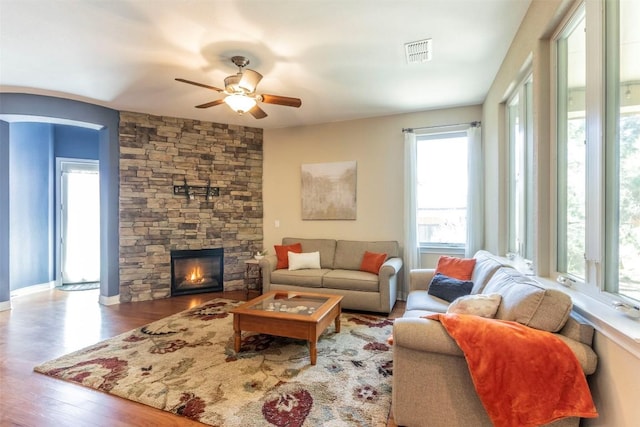 living area featuring visible vents, arched walkways, ceiling fan, wood finished floors, and a stone fireplace