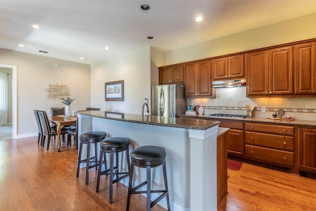 kitchen with stainless steel appliances, light wood-style floors, a kitchen bar, and under cabinet range hood