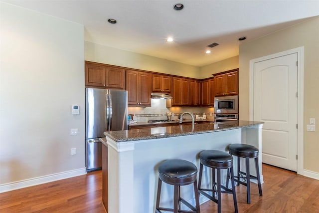 kitchen with tasteful backsplash, dark stone counters, a breakfast bar, stainless steel appliances, and light wood-style floors