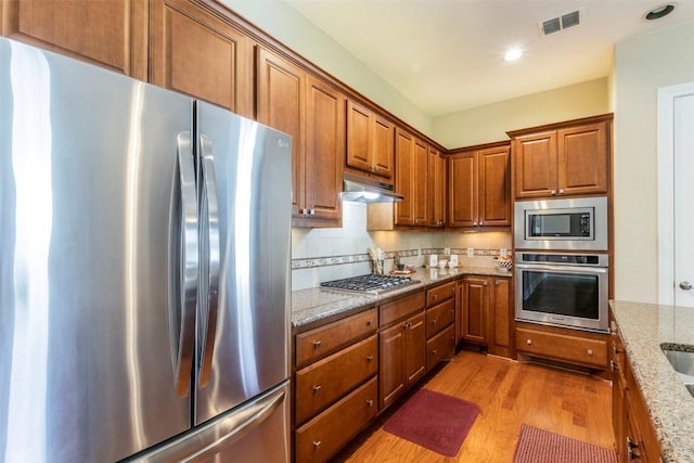 kitchen with stainless steel appliances, tasteful backsplash, visible vents, light wood-style flooring, and under cabinet range hood