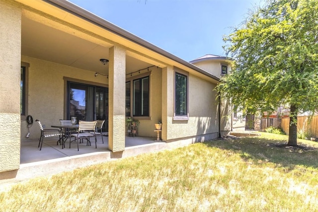 rear view of property featuring a yard, a patio area, fence, and stucco siding