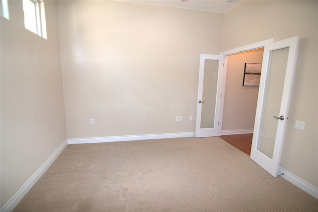 empty room featuring light carpet, baseboards, and french doors