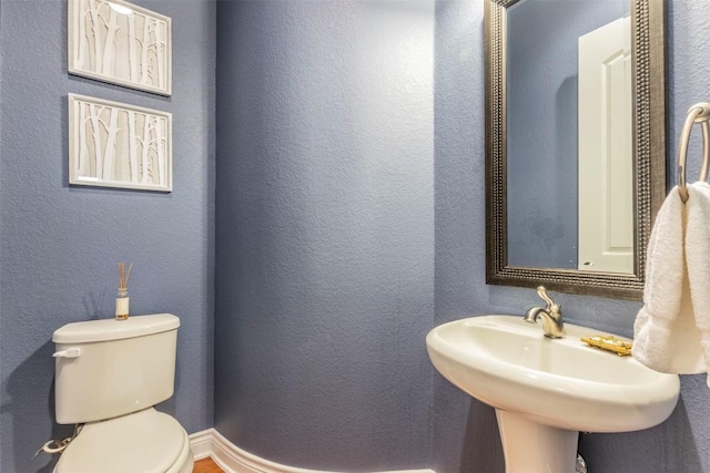 half bathroom featuring a textured wall, a sink, and toilet