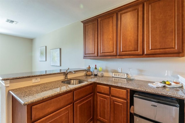 kitchen featuring visible vents, brown cabinetry, a sink, light stone countertops, and a peninsula