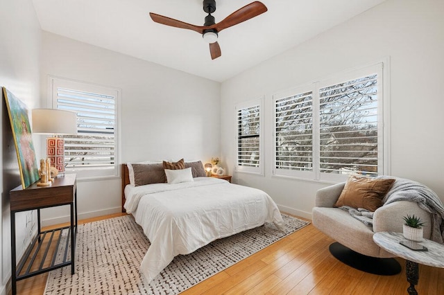 bedroom featuring light wood-type flooring, multiple windows, baseboards, and a ceiling fan