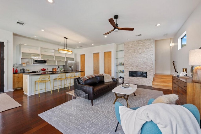 living room with dark wood finished floors, recessed lighting, visible vents, a ceiling fan, and a stone fireplace