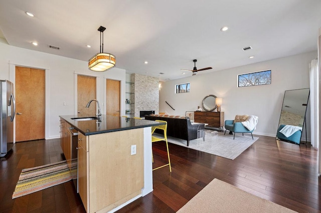 kitchen featuring visible vents, dark countertops, dark wood-style flooring, a fireplace, and a sink