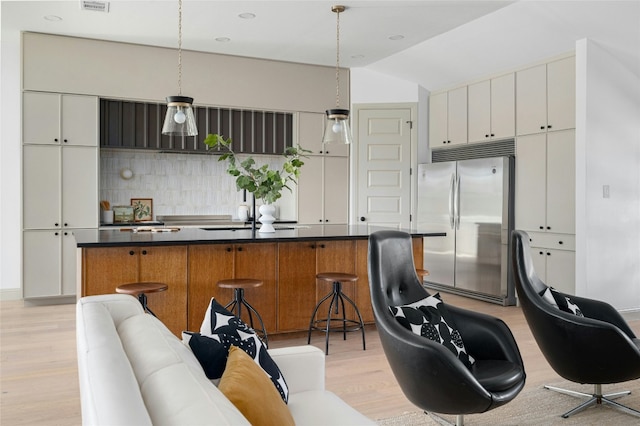 kitchen featuring a spacious island, dark countertops, backsplash, light wood-style floors, and stainless steel built in fridge