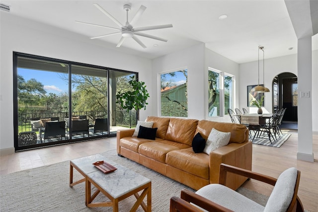 living room featuring arched walkways, visible vents, ceiling fan, and light wood finished floors